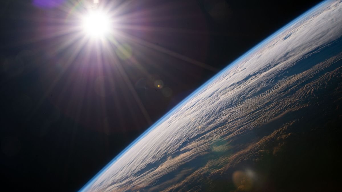 view of the bright sun over the curve of the edge on earth with the thinness of the atmosphere apparent