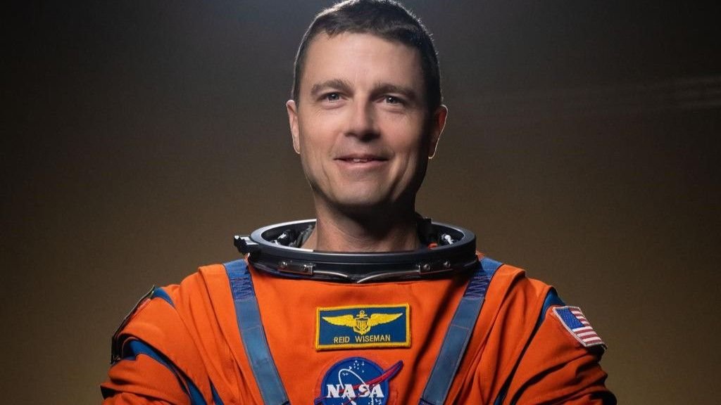 a man wears an orange spacesuit with no helmet