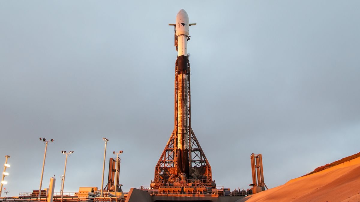 a white and black rocket stands on the launch pad beneath a cloudy sky