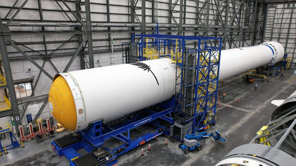 a large white rocket lies on its side in a warehouse like building surrounded by scaffolding
