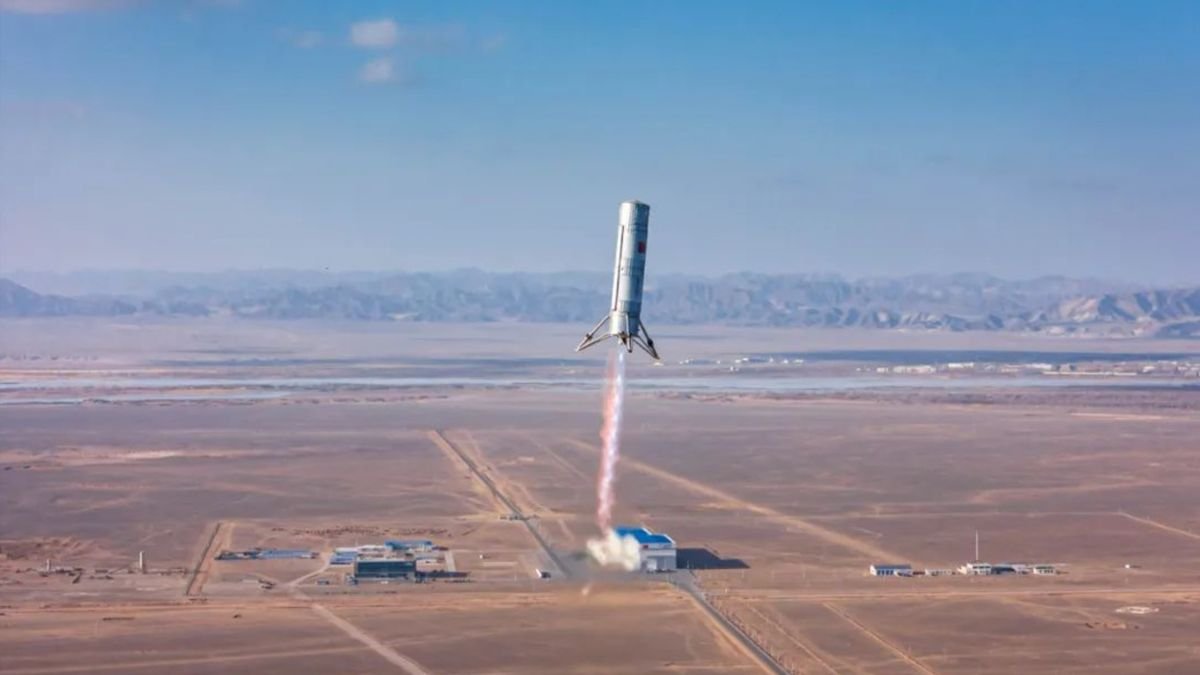 a small silver rocket rises into a blue sky above a desert landscape trailing a pillar of flame