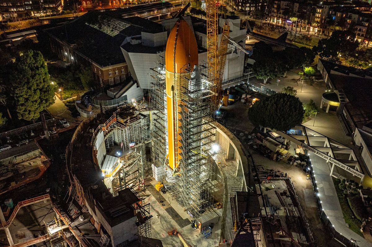a large orange cylindrical tank stands at night surrounded by metallic scaffolding
