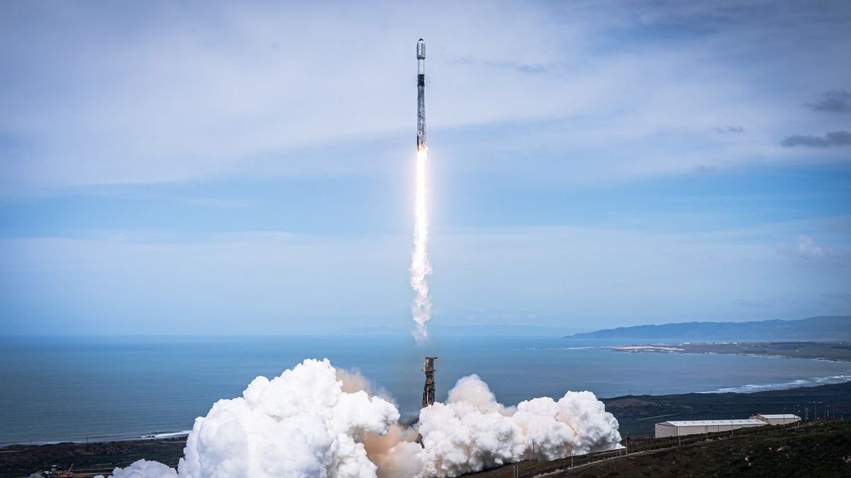 a black and white rocket launches into a cloudy blue sky with the ocean in the background