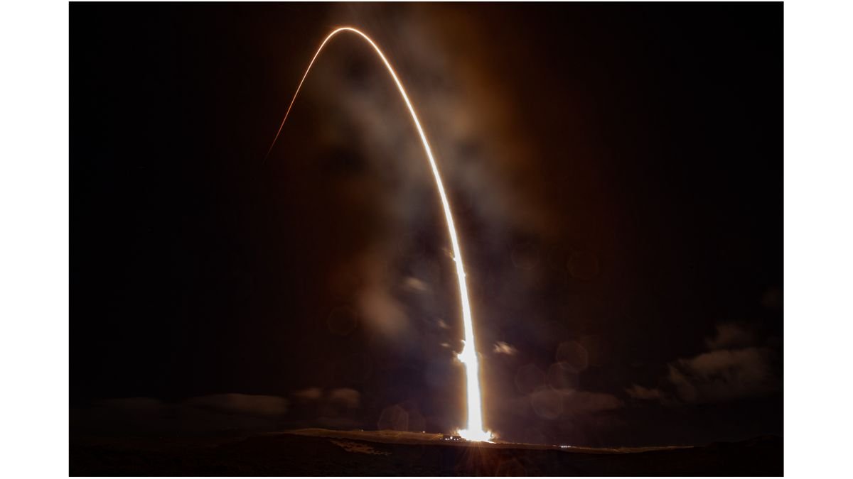 A rocket launch carves an orange arc into a dark night sky in this long exposure photo
