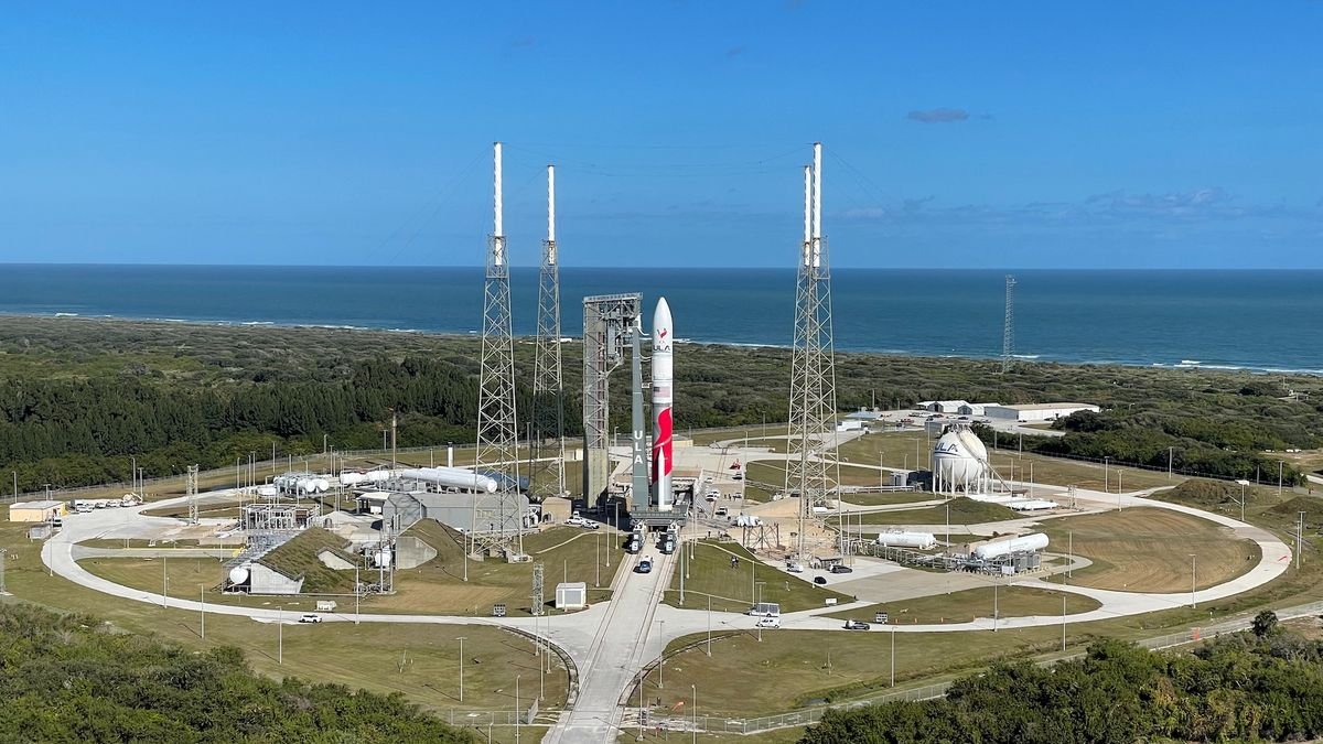 a red and white rocket stands on a launch pad with the ocean in the background