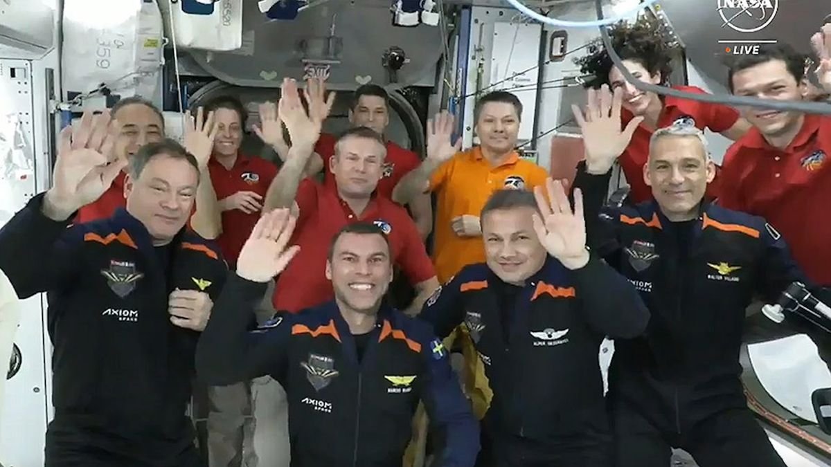 11 people in flight suits wave to the camera aboard the white walled international space station