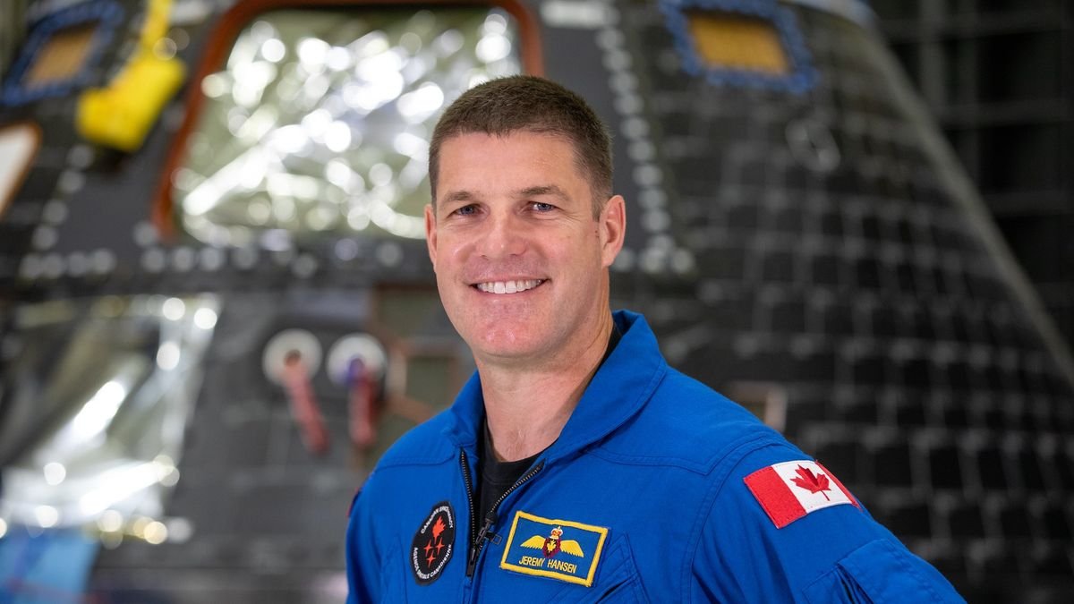 jeremy hansen smiling in front of an orion spacecraft far in the background