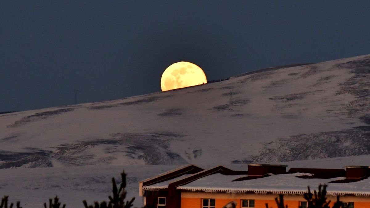 a bright full moon rises behind a snow covered mountain