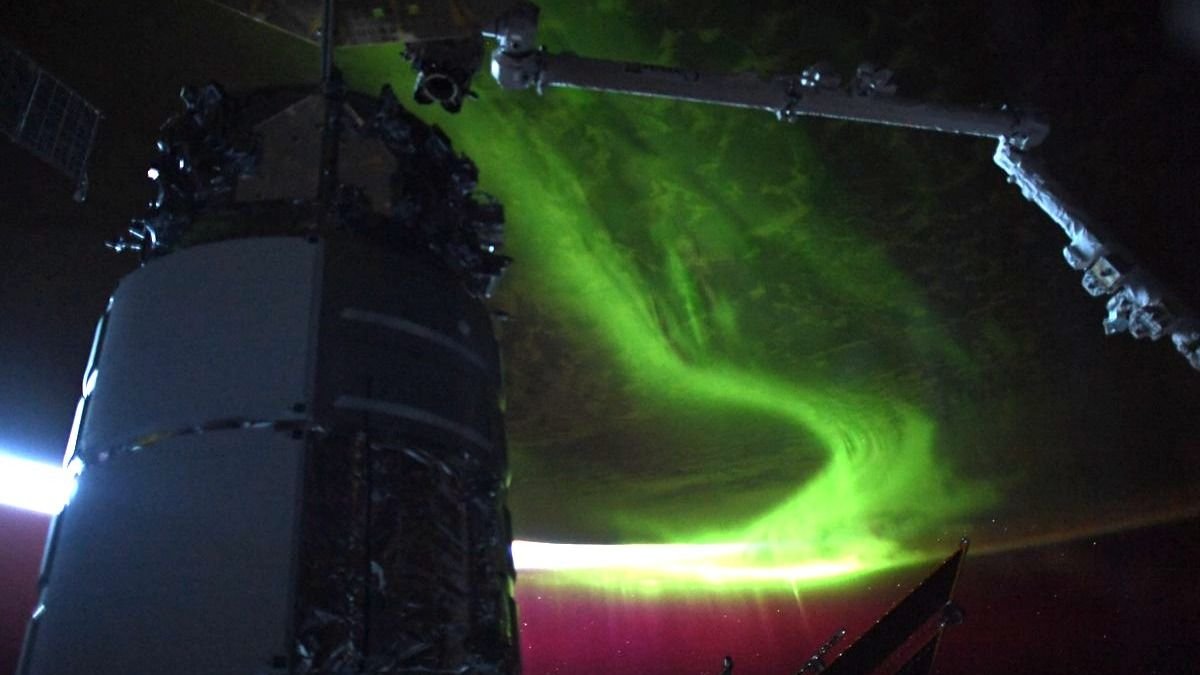 an aurora reaching into space from earth a robot arm and a module are in the front in shadow
