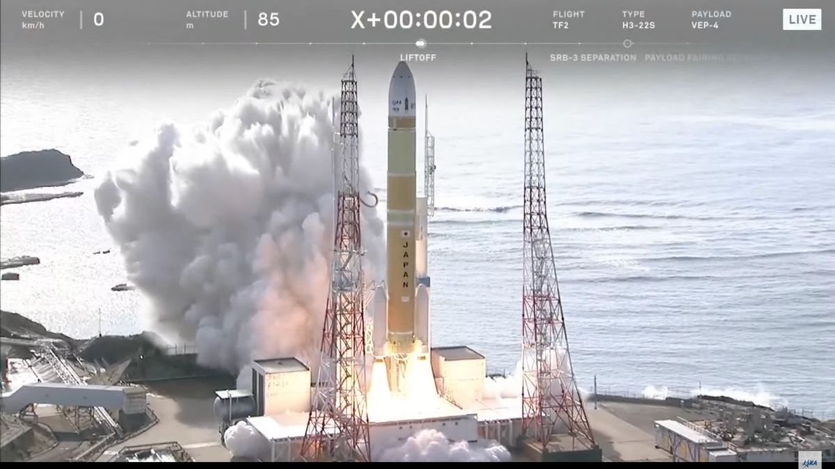 a yellow and white rocket lifts off from a seaside launch pad during the day