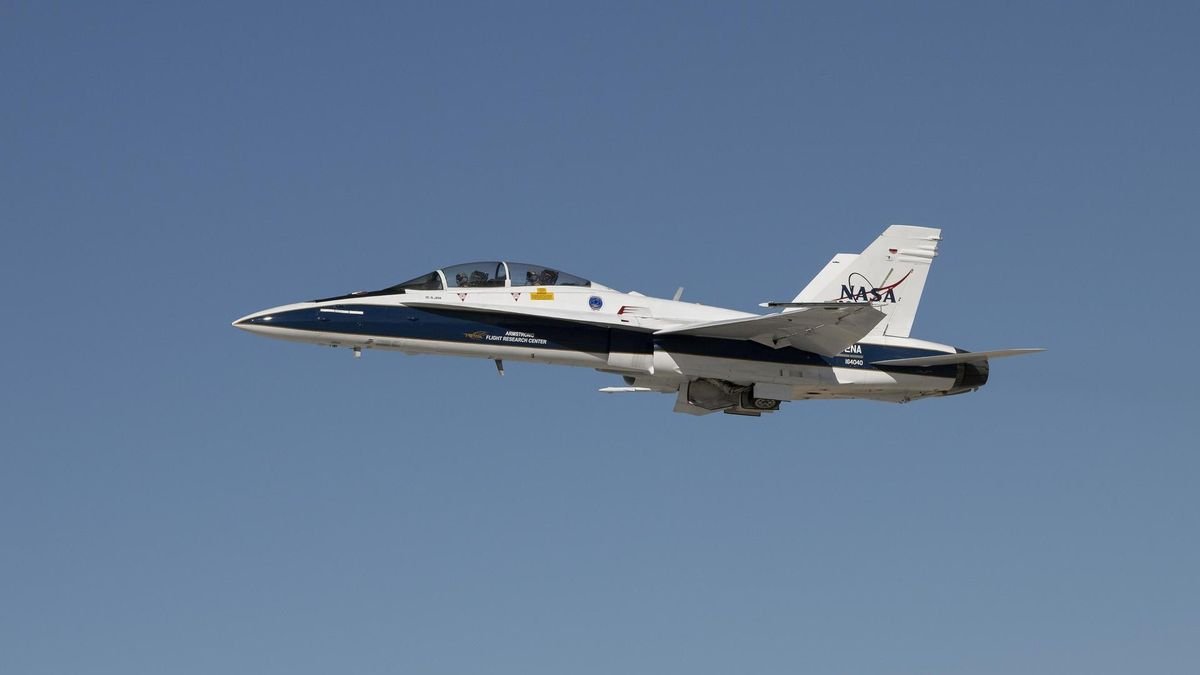 a blue and white fighter jet with the NASA logo flies through open sky