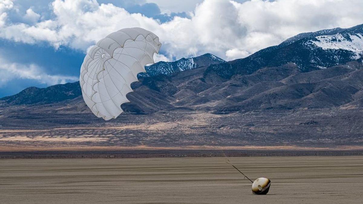 a cone shaped capsule lies on the desert floor with a parachute billowing in the wind above it