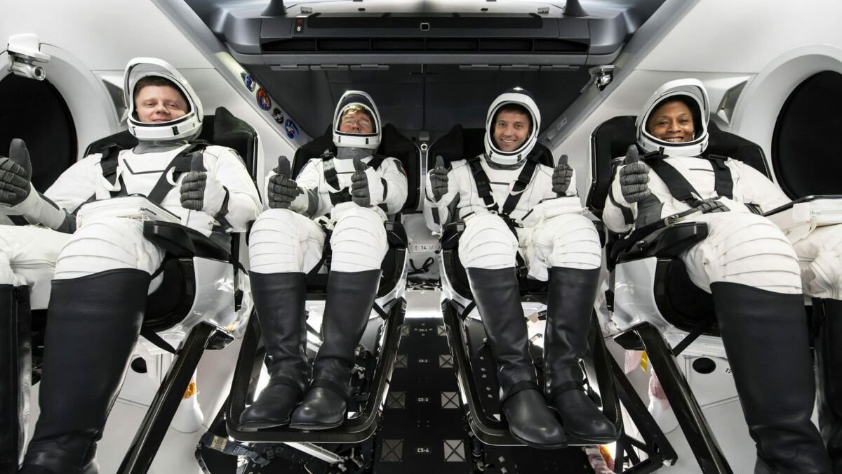 Four astronauts in white launch spacesuits giving thumbs