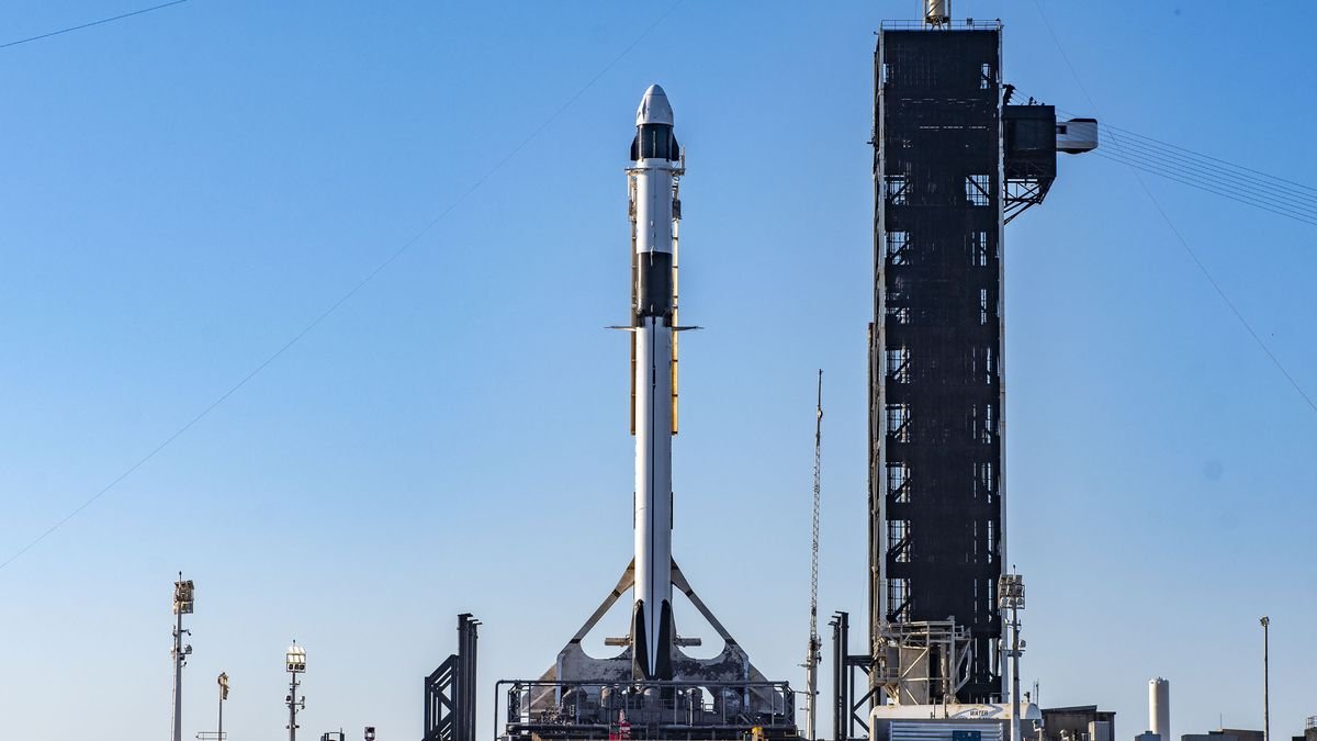 A white and black SpaceX Falcon 9 rocket stands on its launch pad ahead of launch