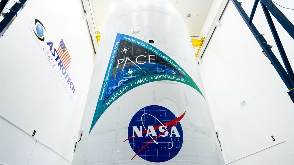 a large white conical payload fairing with logos reading