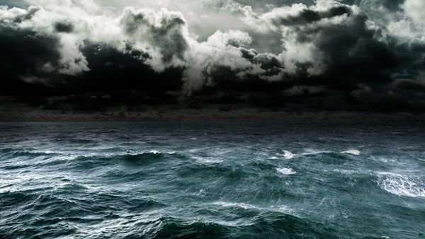 An image of an open oceans surface with crashing waves and a stormy sky