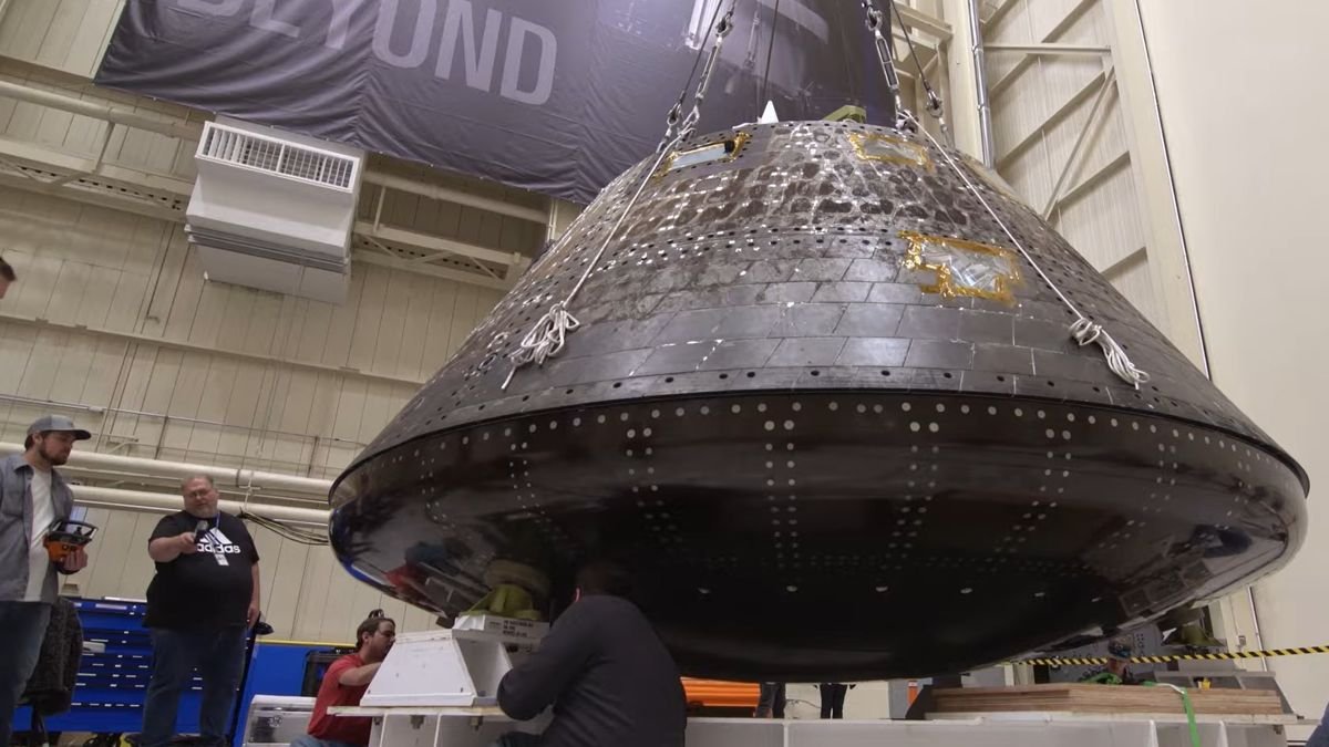 close up of a cone shaped spacecraft in a warehouse with people standing beside it