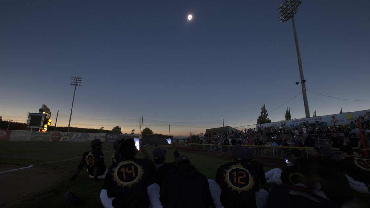 crowds and players gather below to watch the moon eclipse the sun overhead