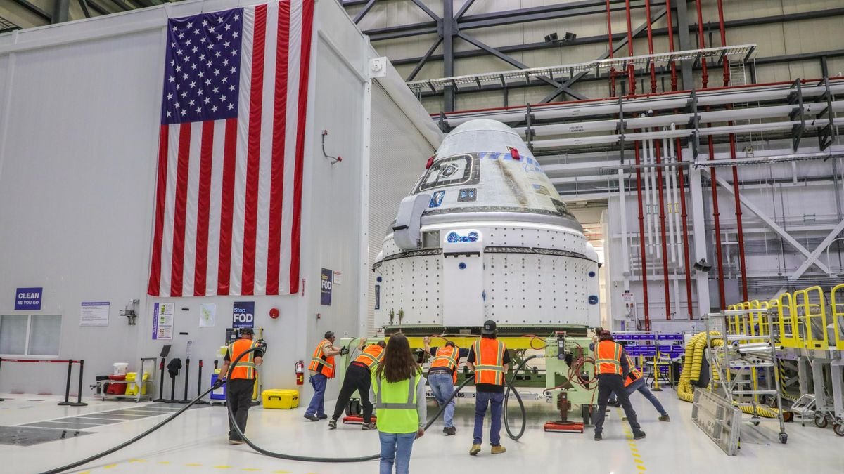 technicians surround a white space capsule in a large room with an american flag on one wall