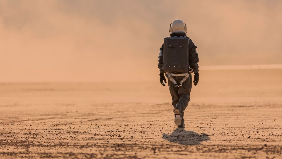 a person in a brown spacesuit walking on a reddish orange desert