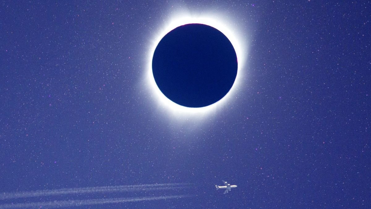total eclipse with white corona and a airplane flying beneath it