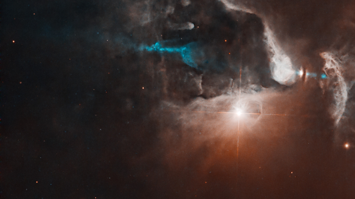 A bright point of light shines near center right with diffraction spikes surrounded by glowing clouds against black space A blue jet of material extends roughly throughout the center of the image partially obscured by the clouds