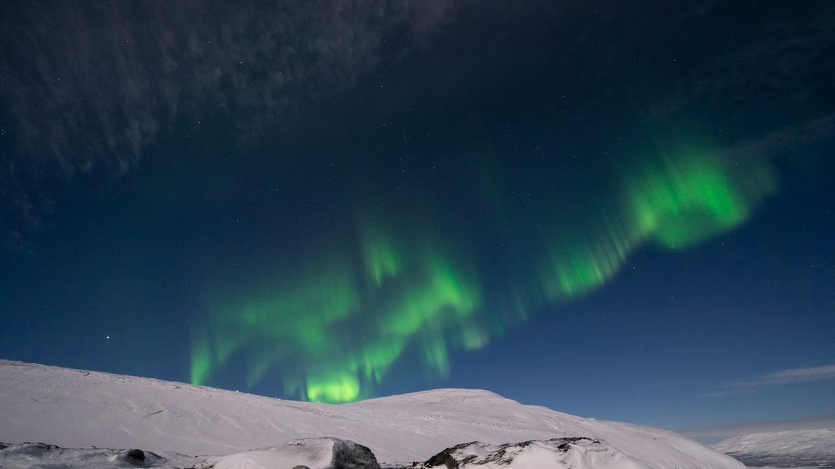 northern lights appear as green ribbons of light across the sky with a snowy mountain below