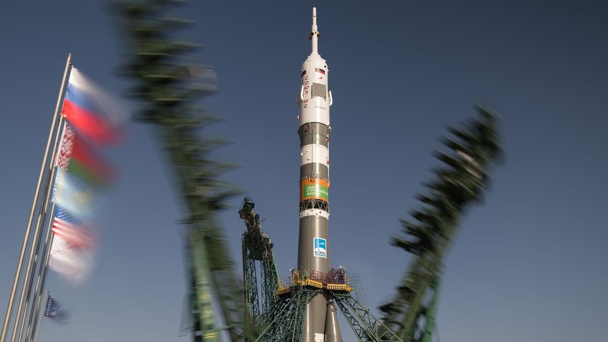 a brown and white rocket stands upright on a launch pad as two metallic skeletal structures fall away from it