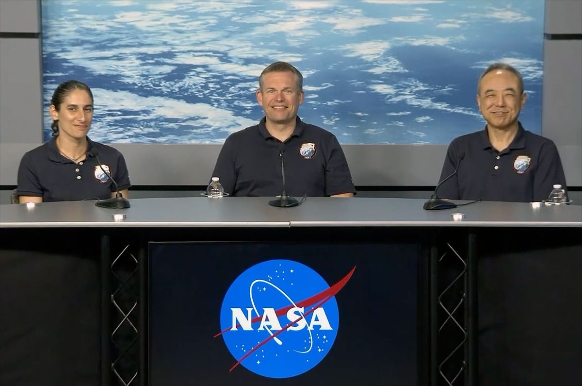 two men and a woman in blue polo shirts sit at a table with a photo of earth as seen from space in the background