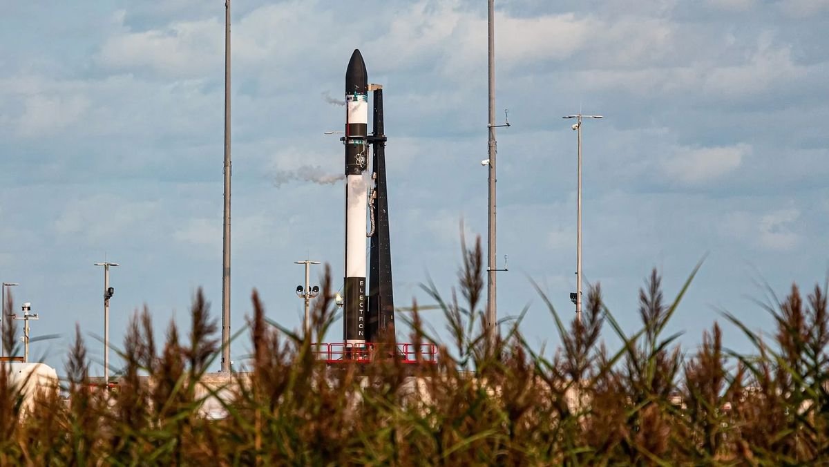 a black and white rocket stands atop its launch pad with high grass in the foreground