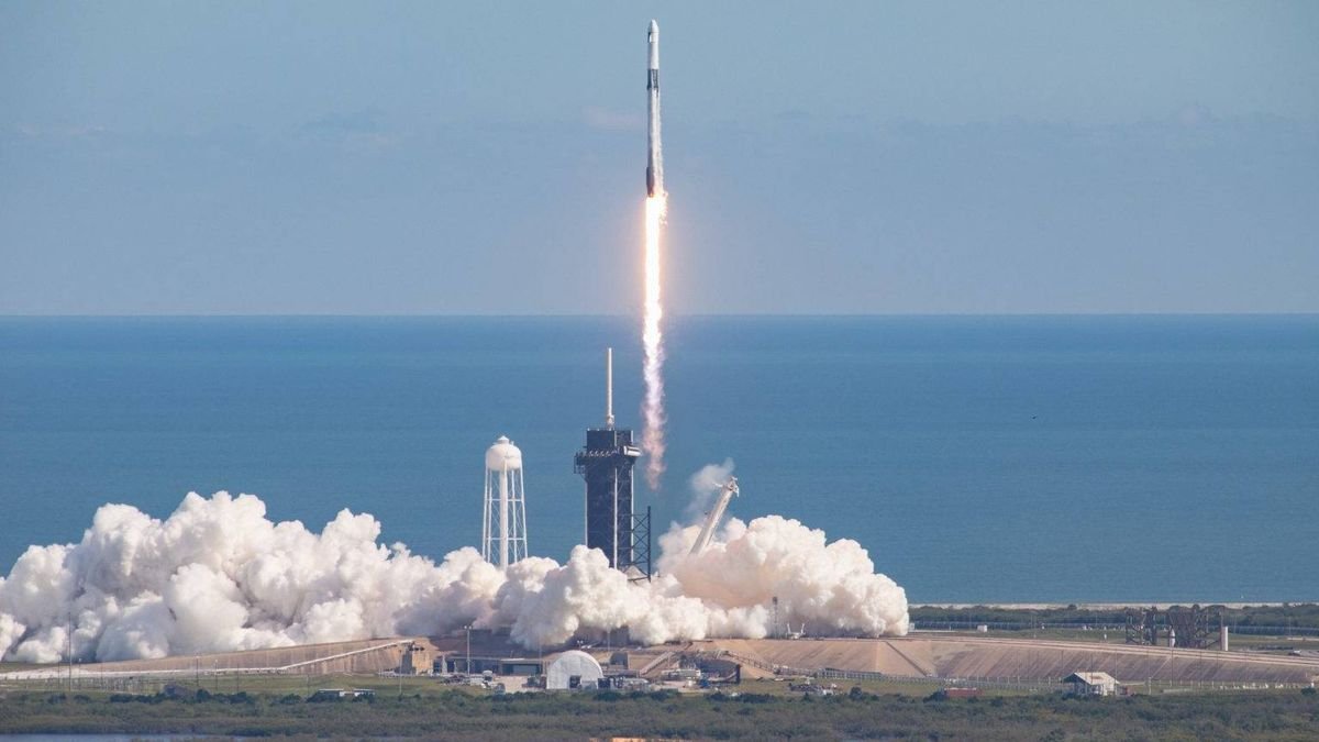 a black and white rocket launches into a blue sky with the ocean in the background