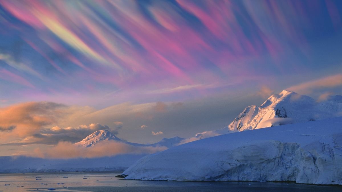 nacreous clouds appear as wispy multi color iridescent clouds streaking across the sky above snowy mountain tops