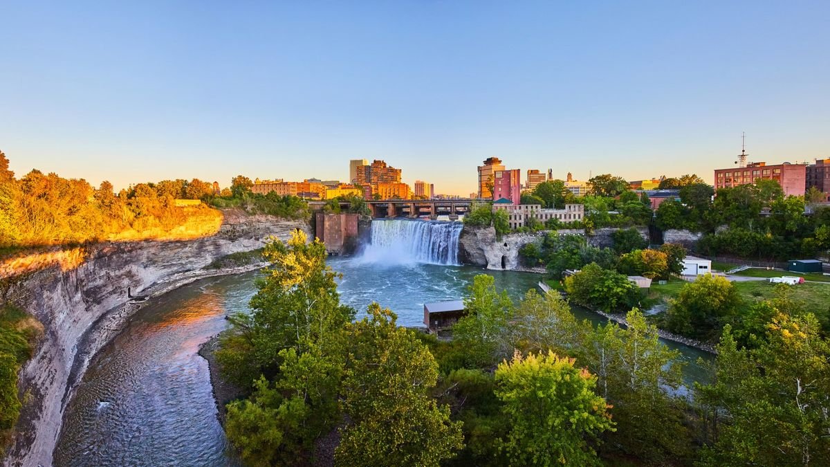 Rochester skyline showing trees and shrubs in the foreground a waterfall in the center and tall buildings in the background