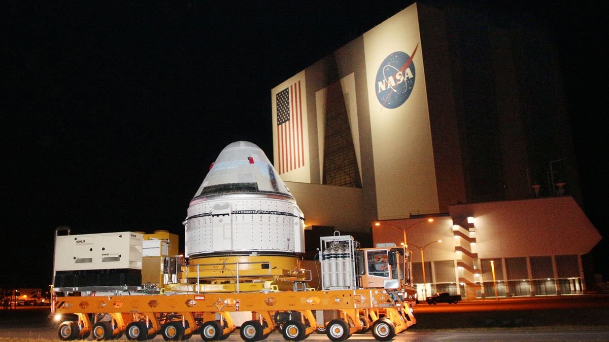 a cone shaped spacecraft on a truck going by a large building with a nasa building on the side the scene is at night