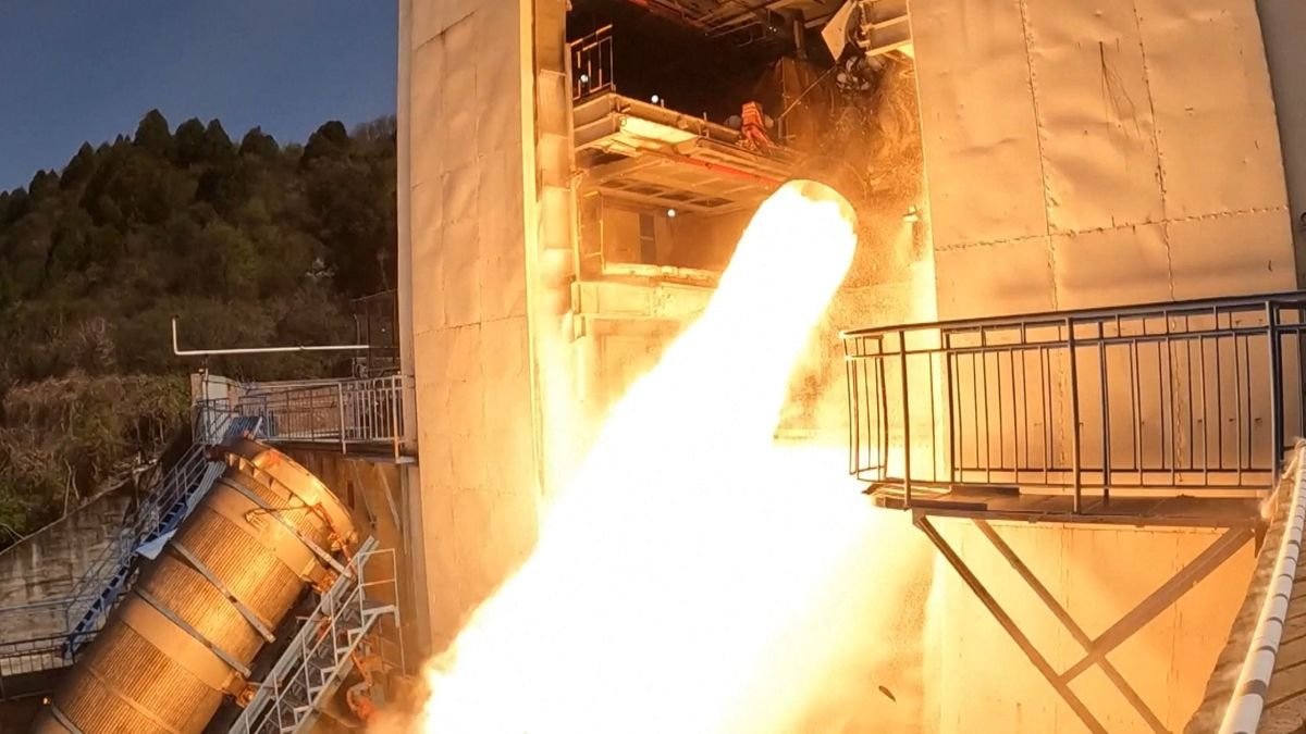 flames shoot out of a cone shaped rocket engine poking out of a hangar like building