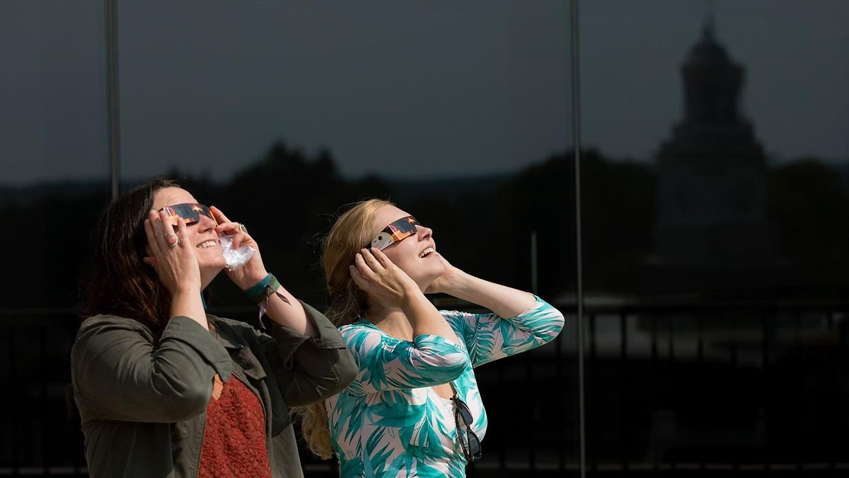 Two women observe the sun with solar eclipse glasses at SUNY Potsdam university