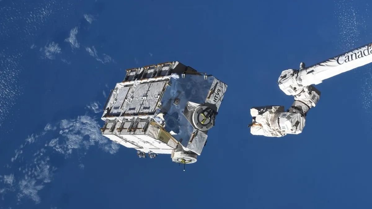 a pallet of silvery batteries is seen in space against the blue ocean of Earth with a white robotic arm to its right
