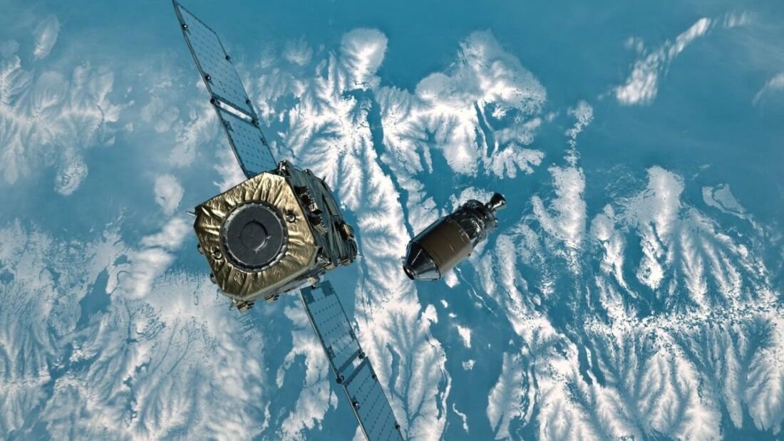 a cube shaped satellite moves toward a spacecraft hovering above some snowy mountains on earth