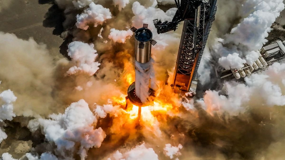 flames billow from the base of a large silver rocket that