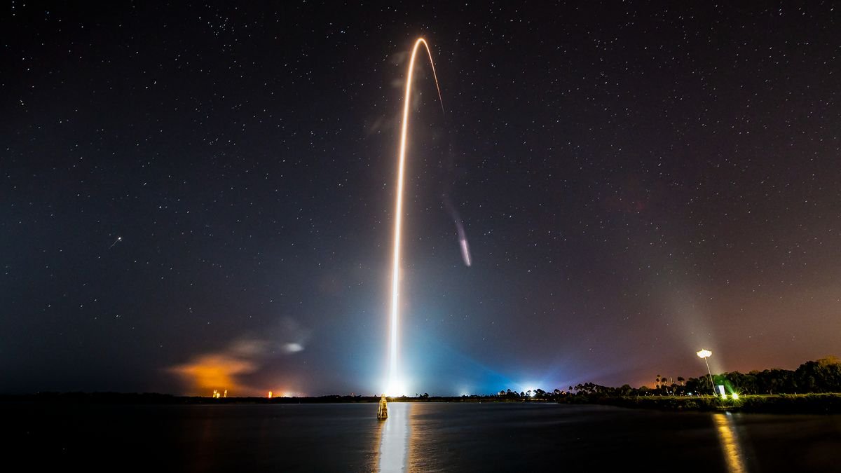 a rocket launch carves a yellow white arc into the night sky