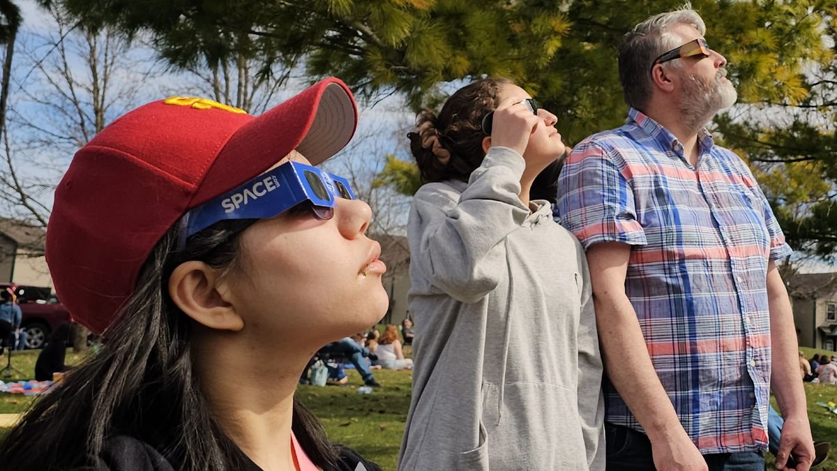 Two girls and a man observe the total solar eclipse of April 8 2024 with eclipse glasses