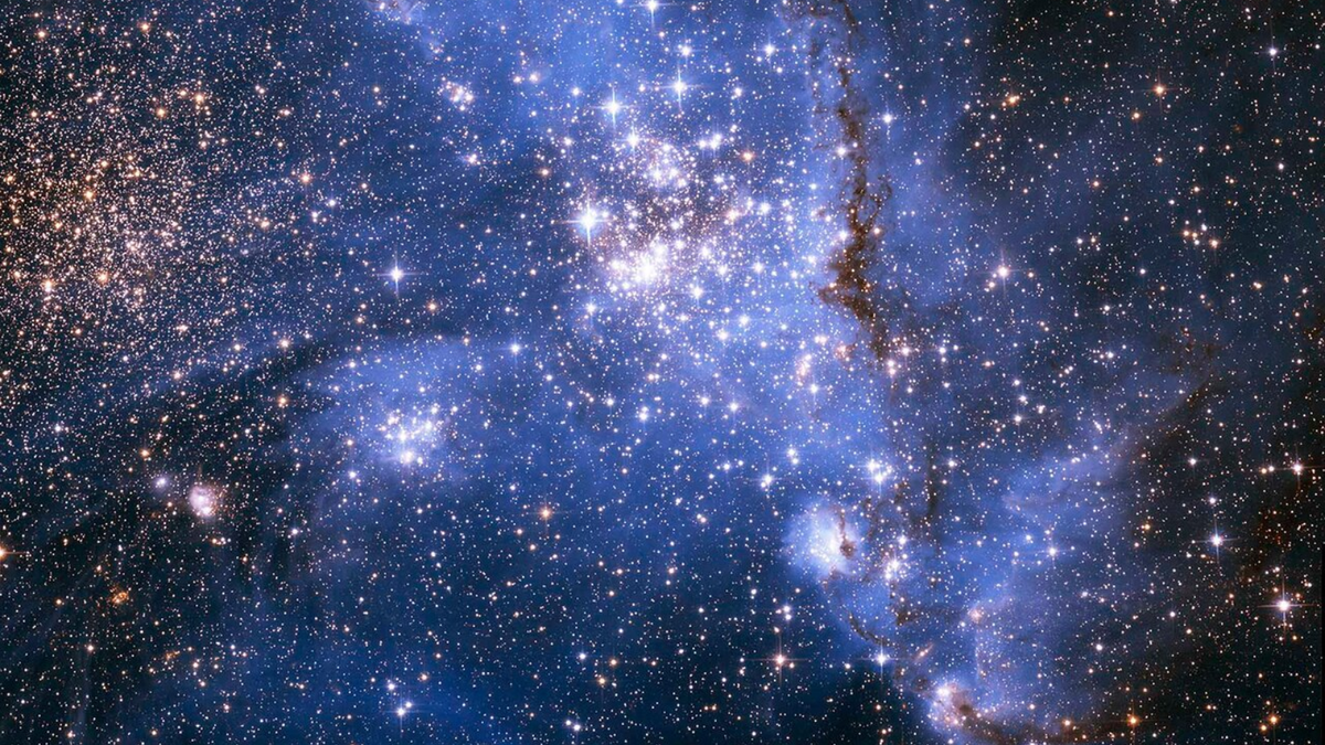 A blue scene of space with lots of stars many of which sparkly quite brightly in the center Streams of gas and other material can be seen as well