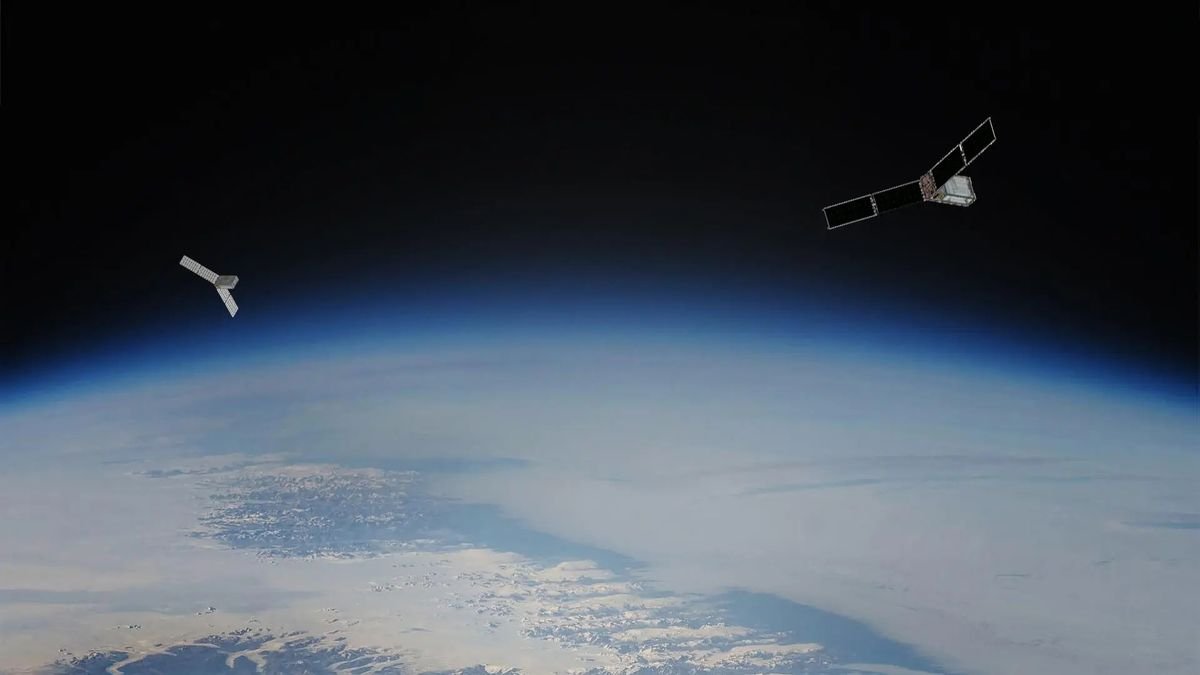 Two small rectangular satellites hover above earth on opposite sides each has a dual panel solar array extended from two sides The curve of Earth below is hazy and blue