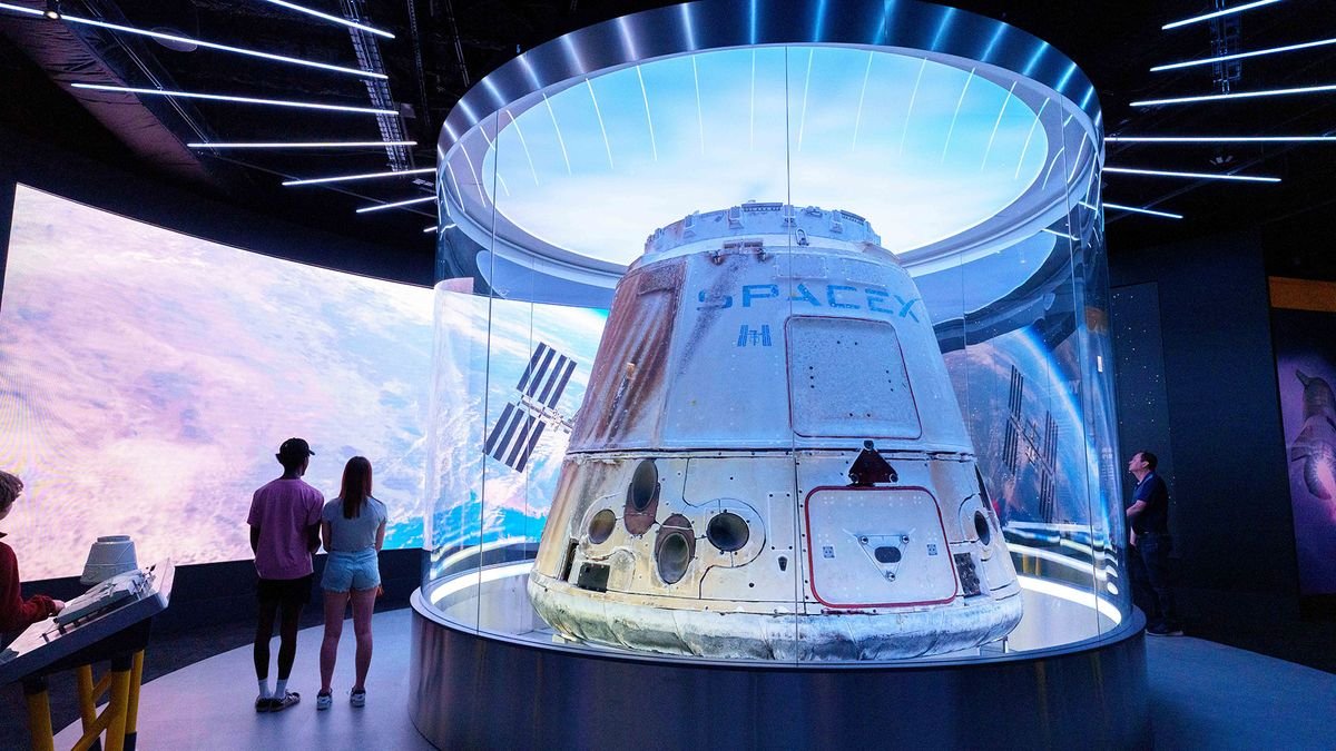 a white space capsule on display in a museum with several people nearby