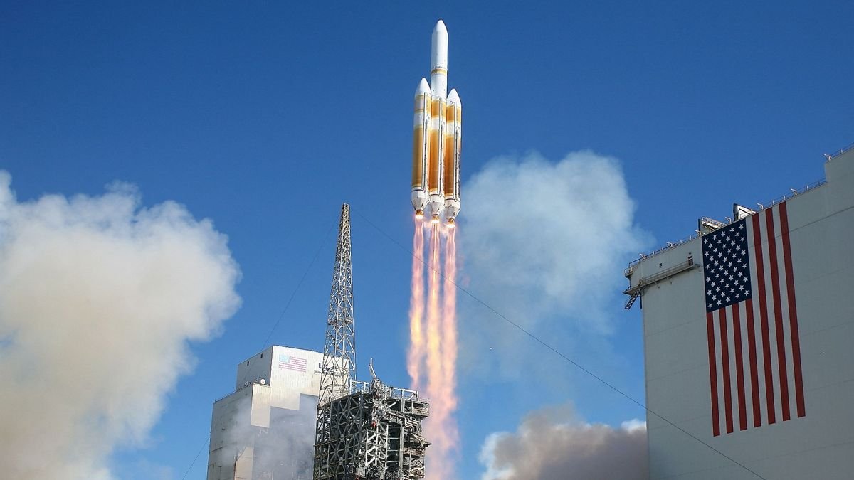 a large white and orange rocket lifts off behind an american flag