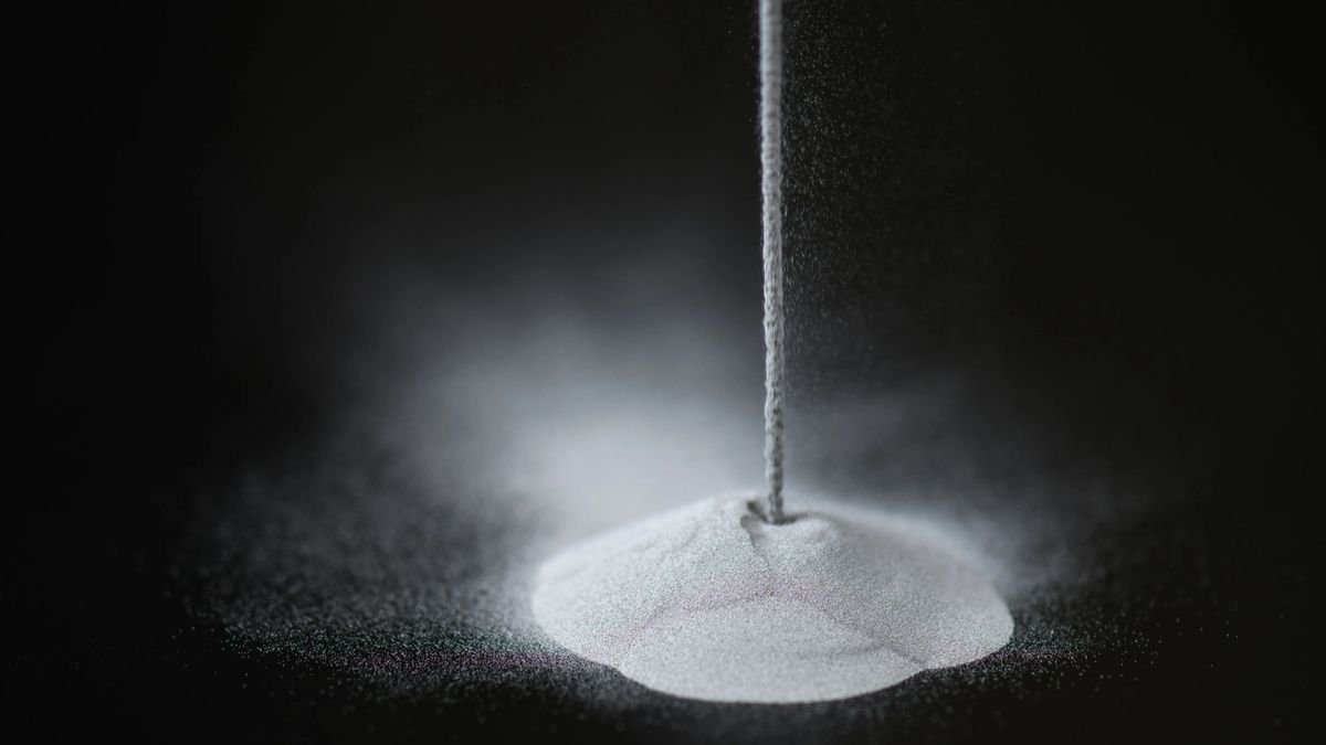 a solid line of a white powdery substance falls from the top just right of center into a pile below on a black surface
