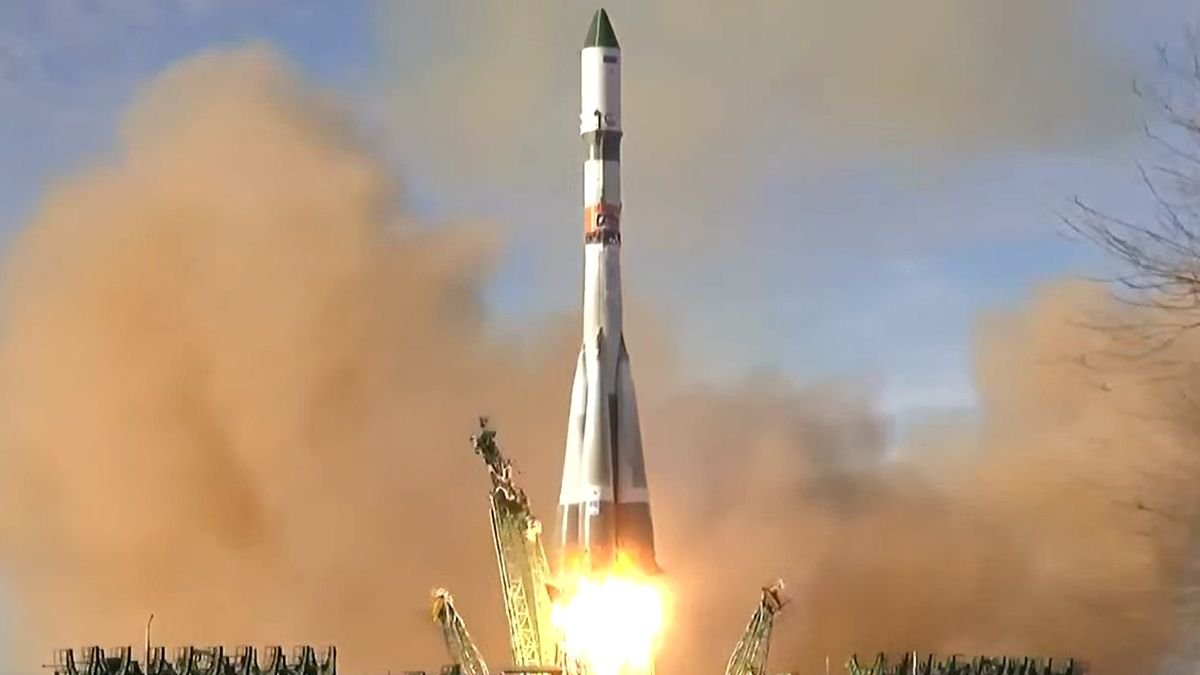 a white red and green rocket launches into a blue sky kicking up lots of dust