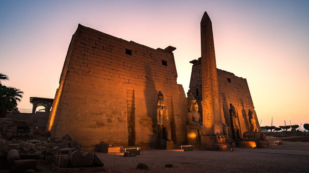 Beautiful sunset at Ruins Luxor temple and obelisk near Nile river at Luxor city Egypt A tall structure is backlit from a rising sun
