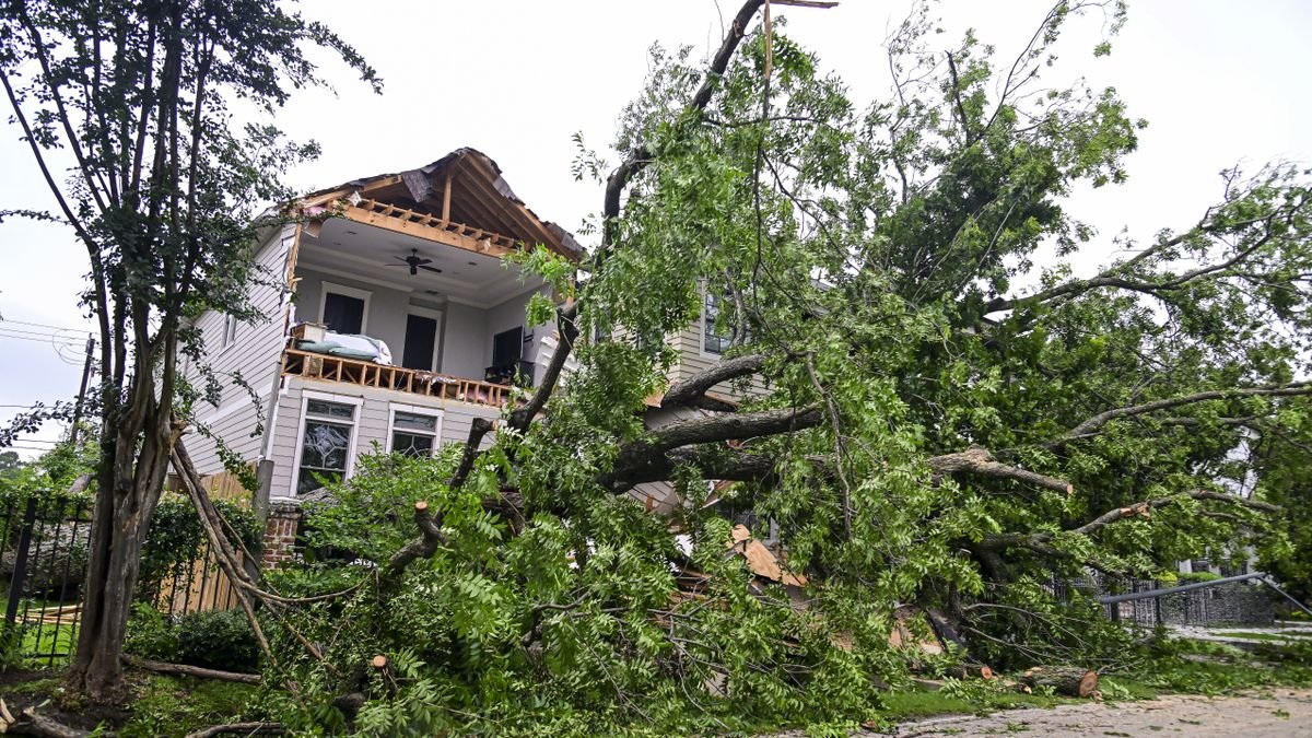 A tree fallen in front of a damaged house against a grey sky