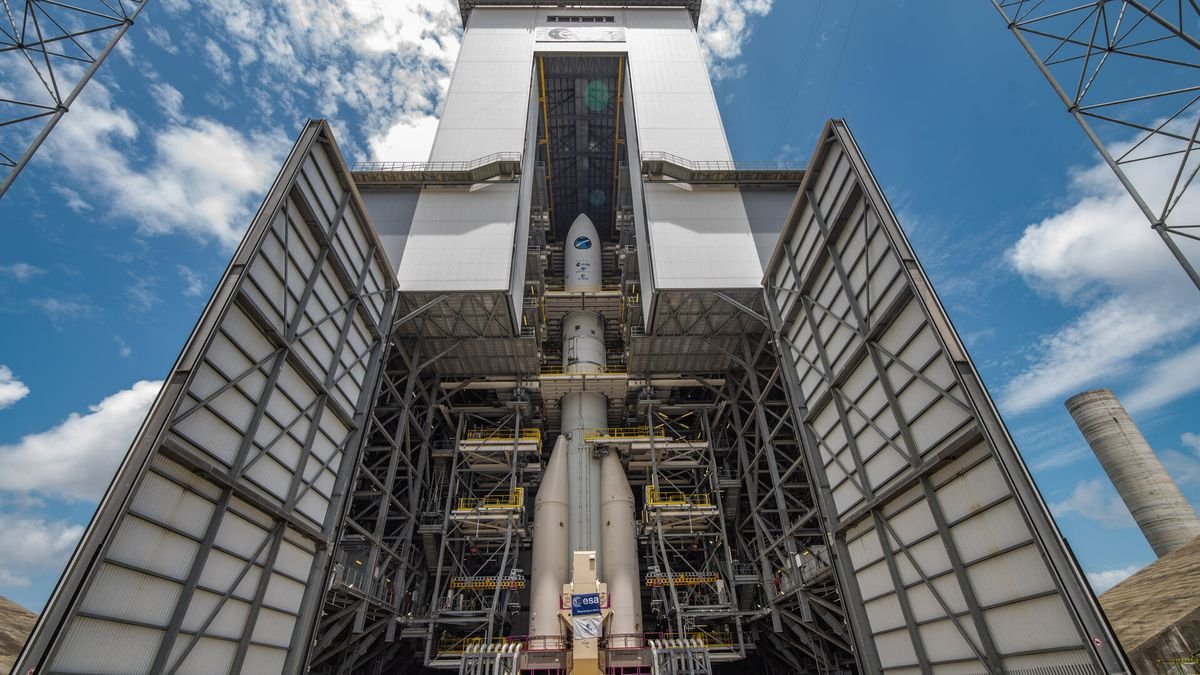 a rocket stands tall in an open assembly hanger before a blue partly cloudy sky